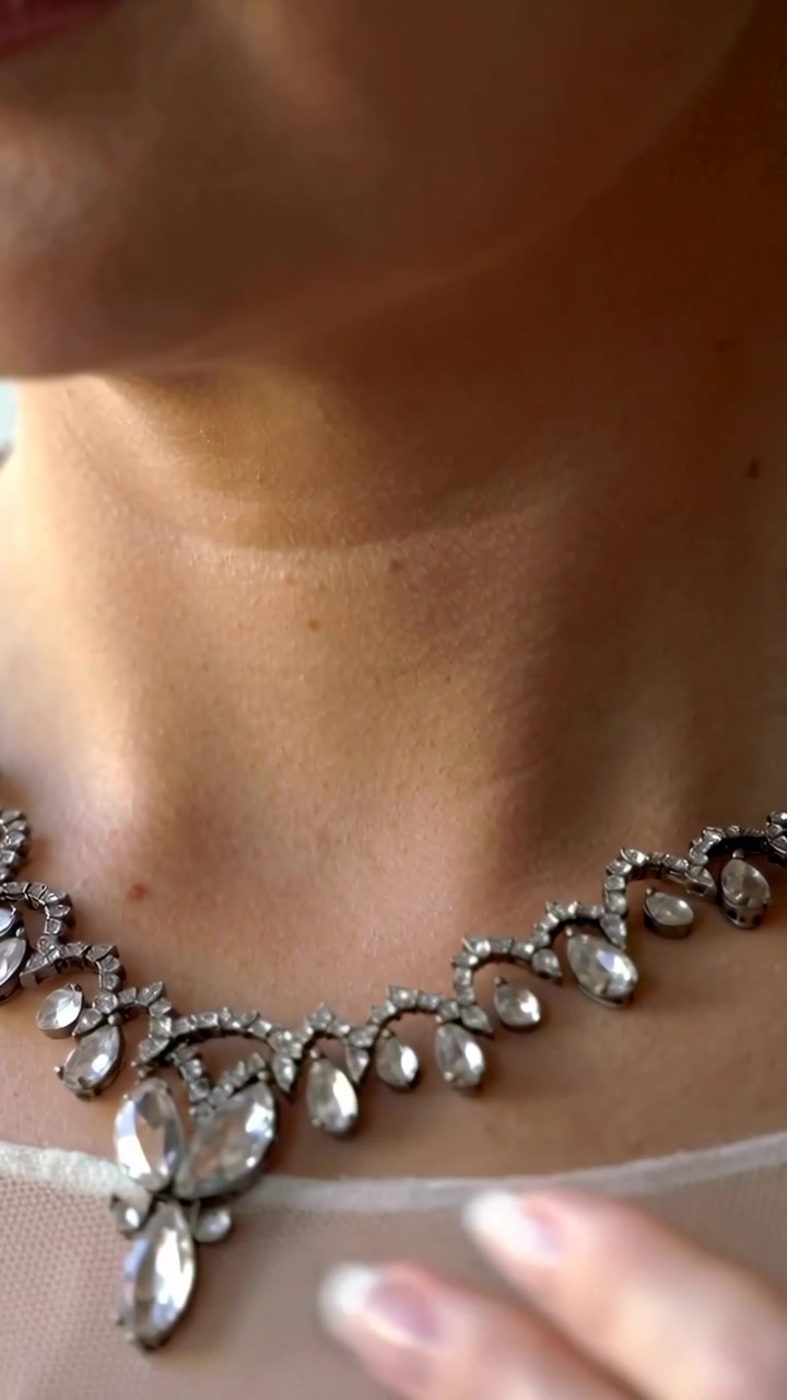 Video verticale: Mani che posizionano una collana di cristallo sulla toeletta, su un top trasparente, centrando il ciondolo