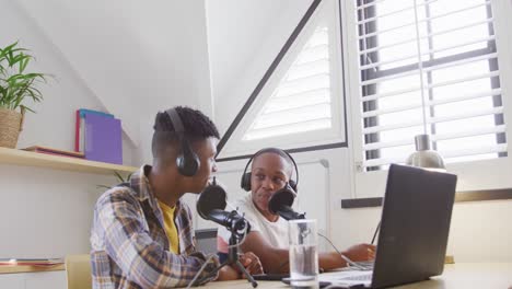 happy african american male teenage friends using laptop and recording podcast, slow motion