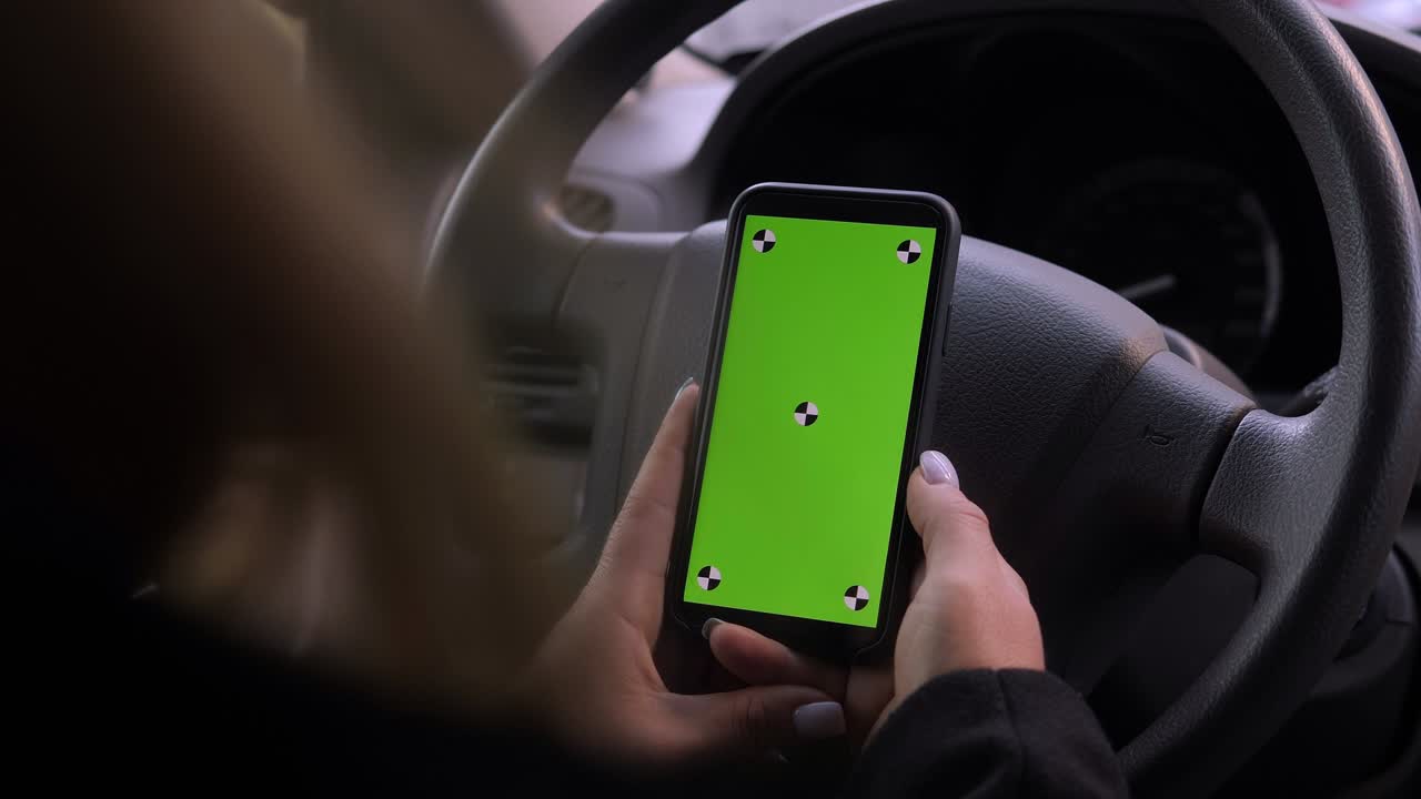 una mujer está conduciendo un coche con un teléfono en sus manos, una llave de croma en la pantalla.