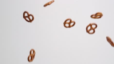 galletas saladas de pretzel retorcidas lloviendo y rebotando sobre fondo blanco en cámara lenta