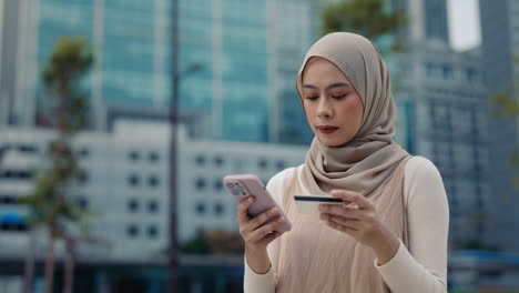 woman using smartphone and credit card in urban setting
