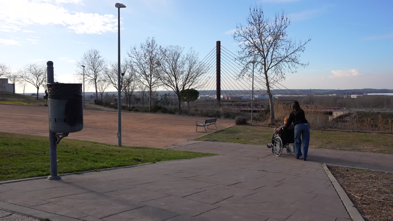 Caregiver carefully pushing elderly person in wheelchair down park slope