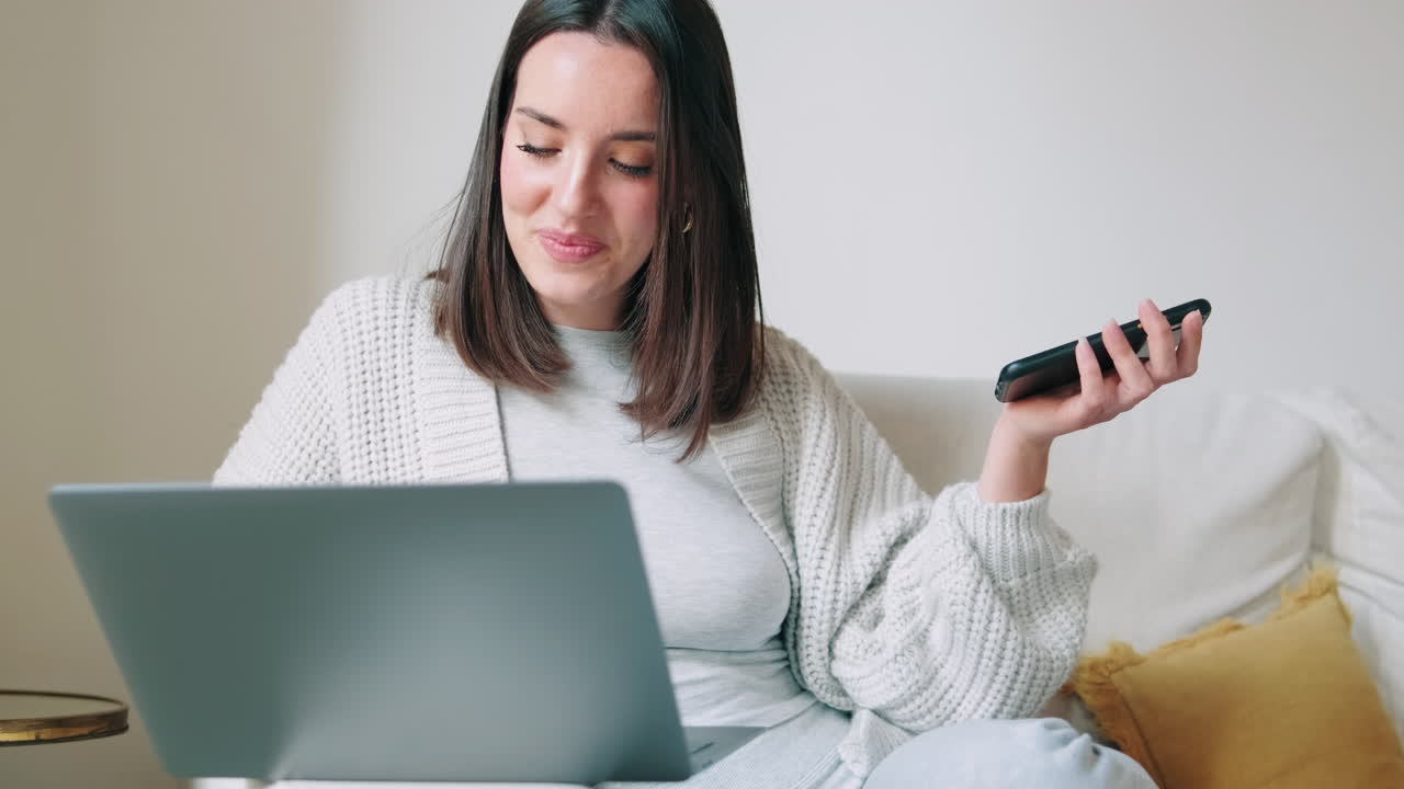 Donna sorridente che fa multitasking con laptop e smartphone sul divano