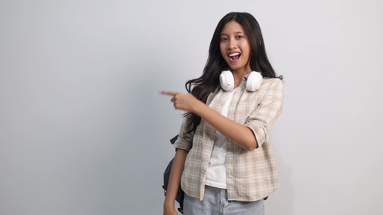Chokeret, forbløffet ung asiatisk universitetsstuderende peger pegefingrene til siden og siger 'wow'.