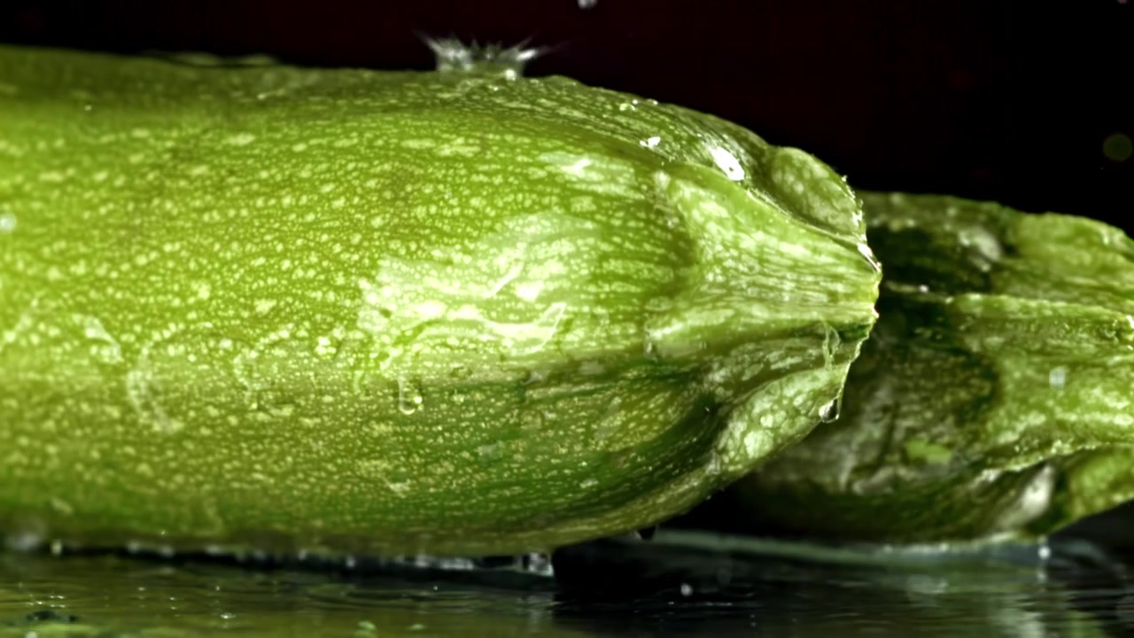 Gocce d'acqua che schizzano su zucchine verdi fresche al rallentatore.
