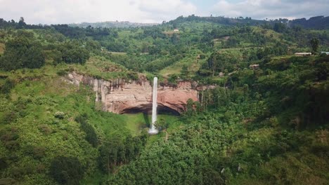 Aerial establishing shot of Sipi Falls cascading from reddish cliffs into lush green vegetation on Mount Elgon’s Park slopes near Kapchorwa, surrounded by farms and forested hills in Uganda.