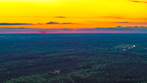 a breathtaking time-lapse captures the setting sun painting the sky in fiery orange and yellow hues above an immense, dense green forest stretching to the flat horizon in rural latvia