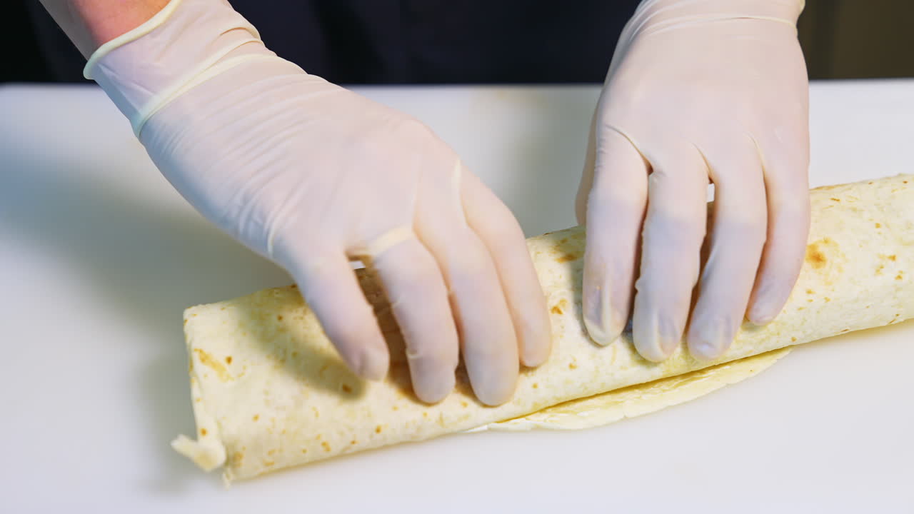Cooking meat and cheese shawarma. Hands in latex gloves roll up a pita roll. Close-up.