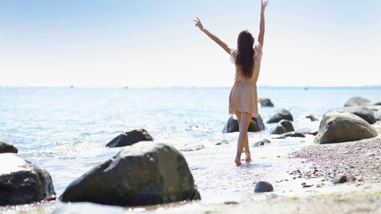 젊고 평온한 여성이 화창한 날 해변에서 걷고 춤추고 미소 짓는다