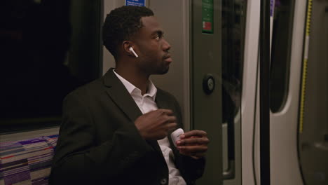 young businessman wearing suit commuting to work sitting in london underground tube train putting in wireless earbuds to stream from mobile phone shot in real time