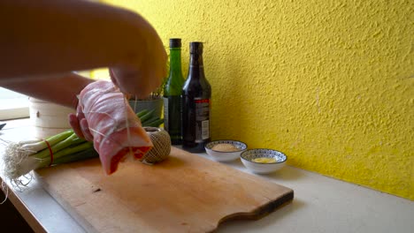 male hands tying up pork belly to a roll with butcher's twine in home kitchen setting