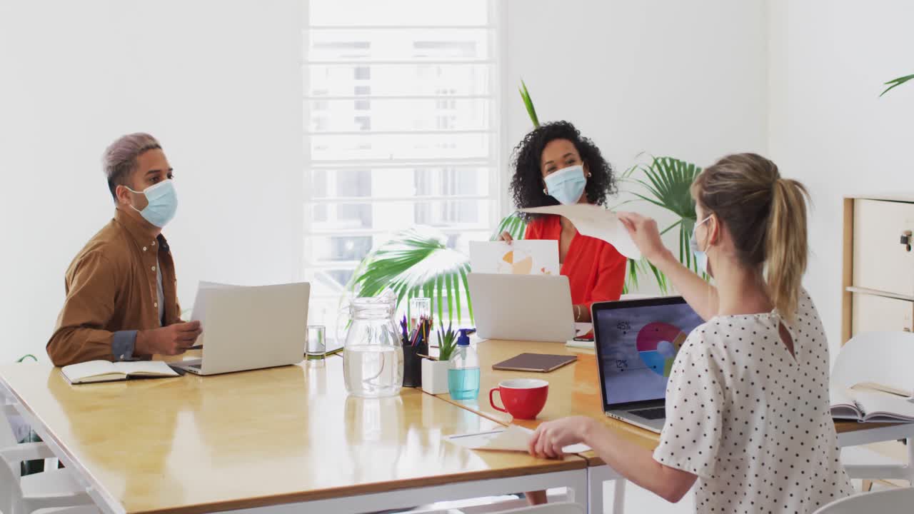사무실 에서 동료 에게 문서 를 보여 주는 얼굴 마스크 를 착용 한 여자