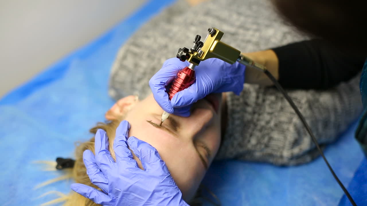 Beautician doing eyebrow tattooing for female face