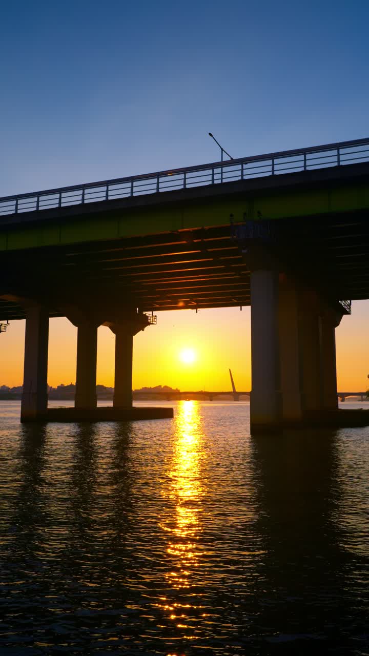 Una splendida inquadratura verticale dal lungofiume mostra il sole dorato che tramonta sul fiume Hangang, incorniciato dalla silhouette del ponte Yanghwa a Seoul, Corea del Sud