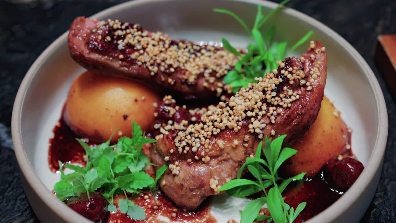 Close up of roasted duck breast plated with caramelized pear, crispy grains, and green herbs
