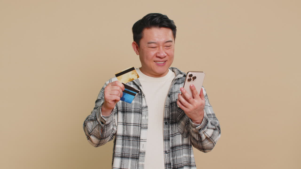 아시아 남자가 신용 카드를 사용하고 스마트폰으로 돈을 송금하며 온라인 쇼핑을 하고 있습니다.