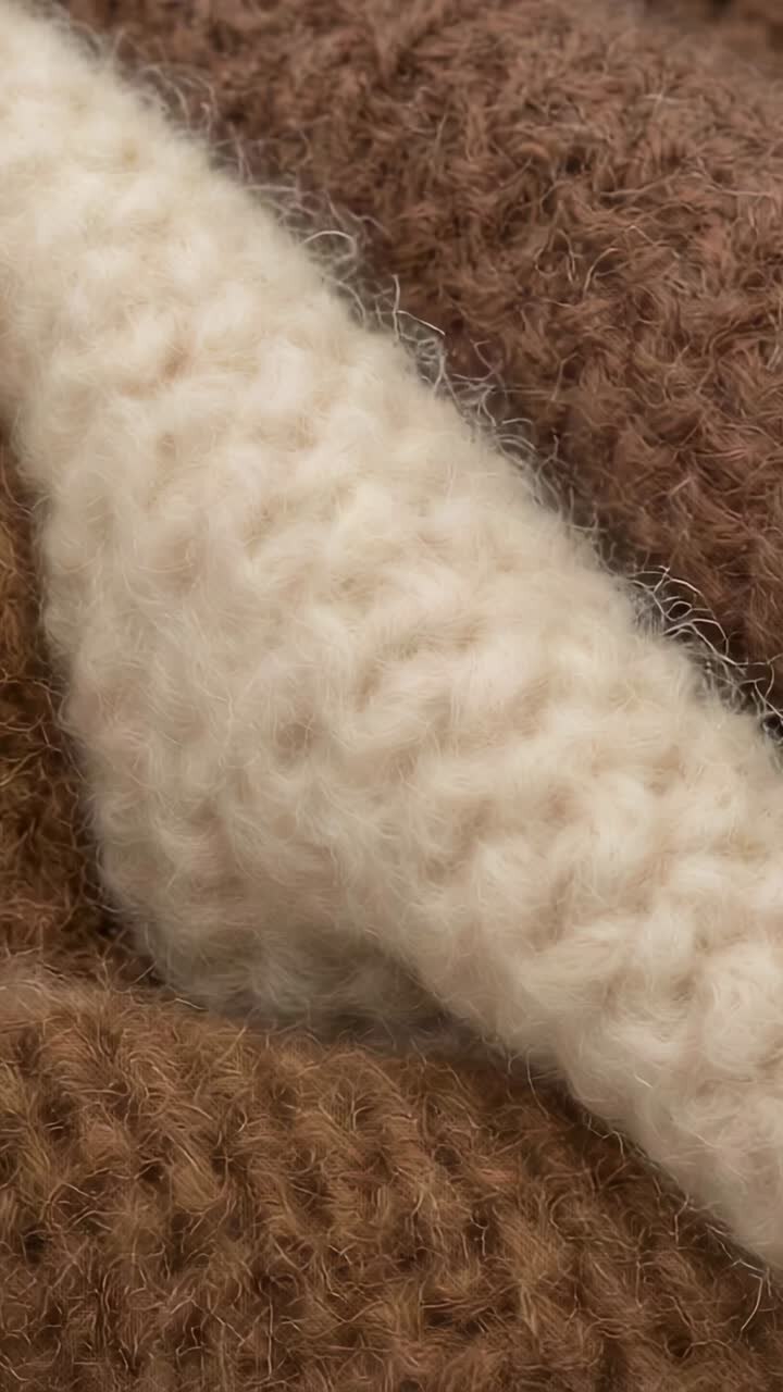 Video verticale: carrellata orizzontale della fotocamera su un tessuto a maglia in studio, che mostra i dettagli dei punti color crema e marrone