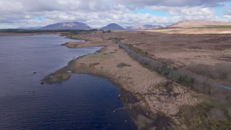 aerial flyover shot coastal road in ireland with lake and dry shoreline. irish landscape with mountains in background. wide shot.