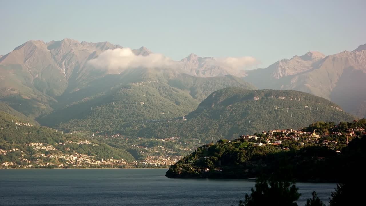 un tiro cerrado otro al lado superior del lago como que muestra olgiasca y gravedona ed uniti a través del lago. en las cimas de las montañas al otro lado de los lagos hay algunas nubes de bajo nivel.