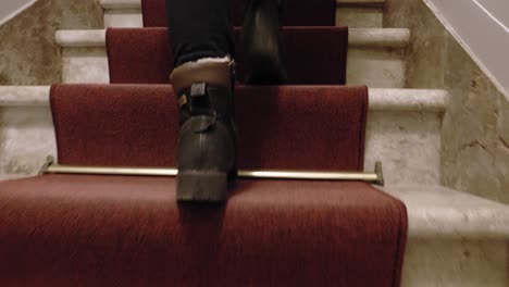 Female-legs-in-boots-climbing-on-the-indoor-staircase-with-red-stair-runner