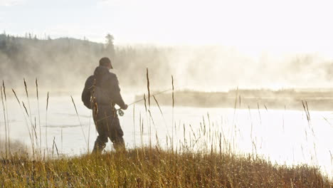 un pescador caminando hacia el río durante la niebla de la mañana