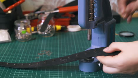 Worker-fixes-silver-eyelet-parts-on-black-leather-belt