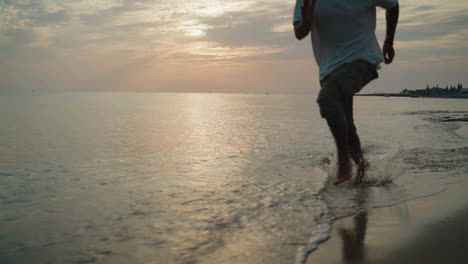 Junger-Mann-Läuft-Am-Strand-Im-Wasser-Bei-Sonnenaufgang-In-Superzeitlupe