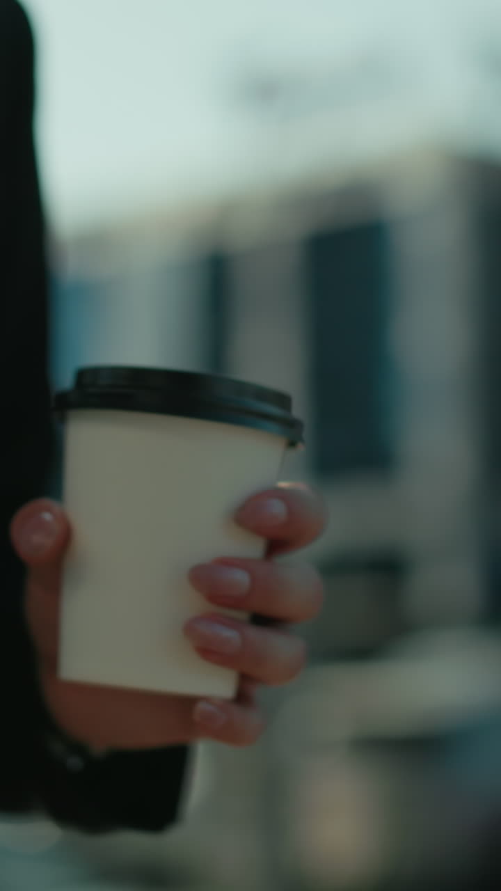 Close up of young girl in business outfit walking while holding tea cup under daylight, cityscape with bokeh lights, parked cars, and urban background