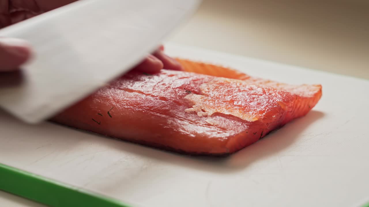 un chef japonés profesional corta una rebanada de salmón ahumado con un gran cuchillo de plata.