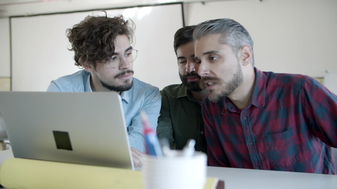 Front view of focused young people sitting at table and looking at laptop