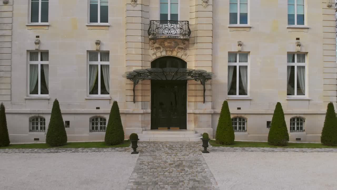Medium aerial dolly-up shot revealing the ornate façade of a historic French-style building with tall windows and elegant details