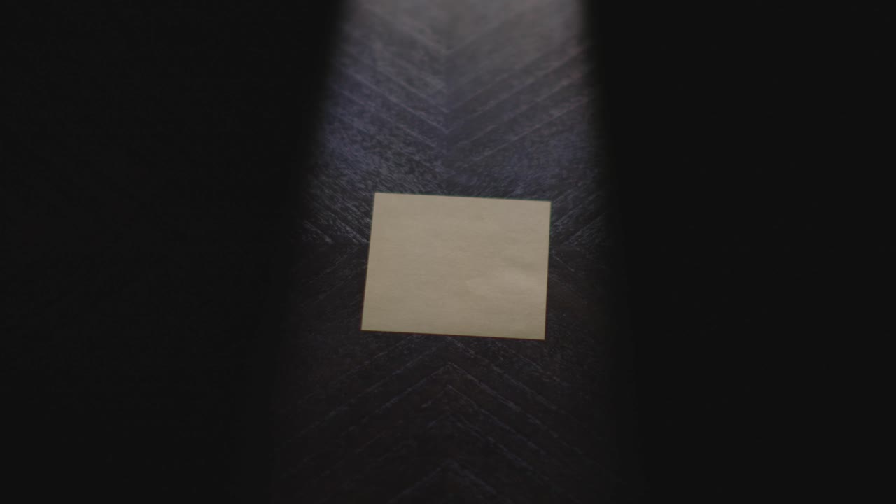 Slow motion close up footage of a hand writing out "August" on a paper note and placing it on a table. Shot in dramatic lighting for an impressive title or transition