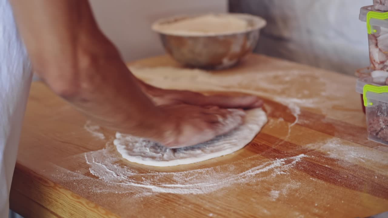 Baker kneading dough in flour on table. Hands of professional bakery chef on dough. Man forming dough of a round form for pizza.