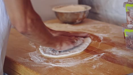 baker kneading dough in flour on table. hands of professional bakery chef on dough. man forming dough of a round form for pizza.