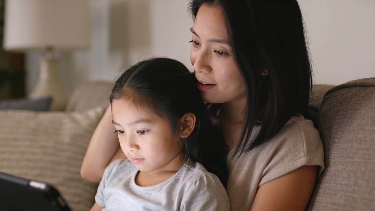点灯したタブレットに応答する、自宅のソファに座る母親と子供。母親は子供の頭をなで、二人とも薄手のシャツを着ている。