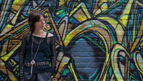 retrato de moda al aire libre de una mujer joven de estilo alternativo apoyándose en una pared cubierta de graffiti en la calle de la ciudad de londres, reino unido, en tiempo real.