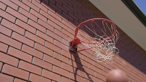 side perspective of basketball circling around basketball ring in slow motion before going through net for a goal with red brick wall background