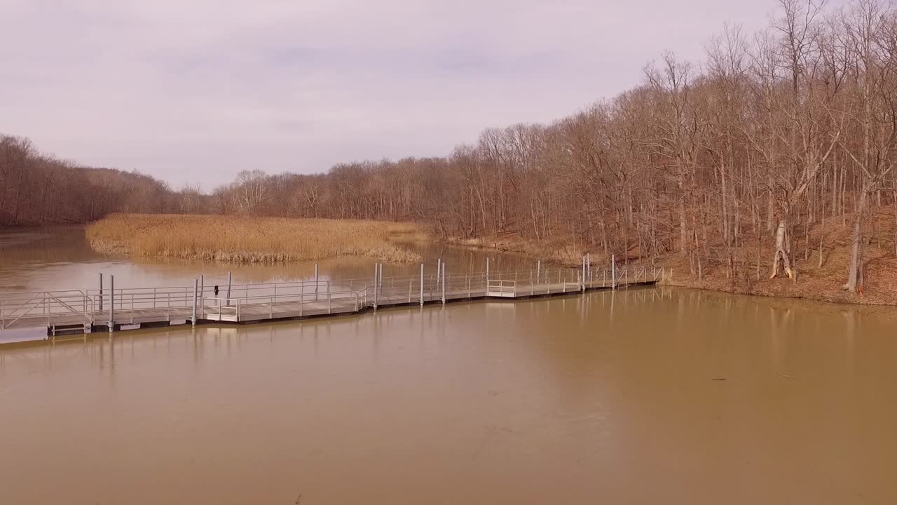 imágenes aéreas de un puente peatonal que cruza un lago helado durante el invierno en un parque estatal