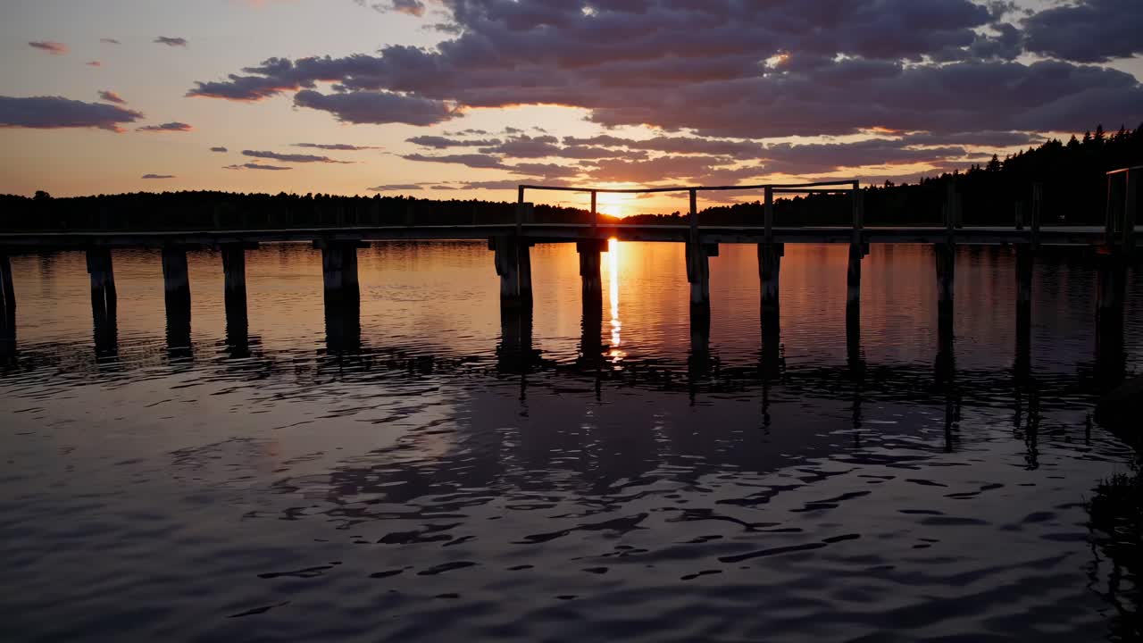 Serene sunset over a lake with a silhouetted pier, captured from a low angle