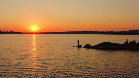 people fishing at sunset. beautiful orange sun on the evening sky. silhouette fisherman with fishing rod catching fish on the stone in water. men relax near the water.