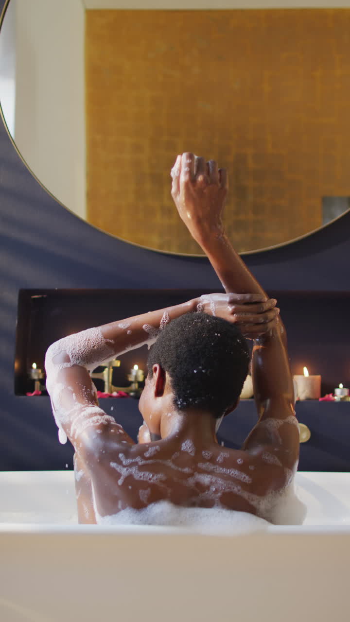 Vertical video of happy african american woman enjoying pampering herself in foam bath
