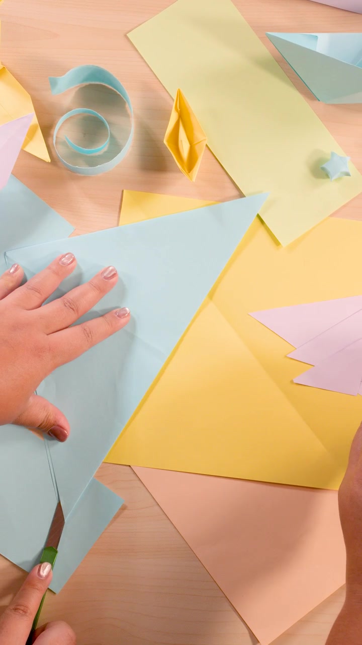 Mani creano origami usando carta colorata, forbici e pieghe precise sotto un'illuminazione morbida e uniforme