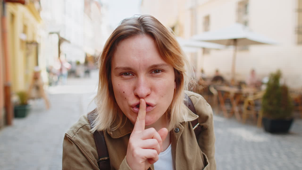 Young woman makes silence hush gesture sign asking do not tells gossip secret on urban city street