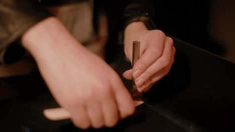 Woman's-hands-using-a-hammer-and-a-leather-chisel-in-the-workshop,-punching-holes,-dark-setup,-high-contrast,-close-up