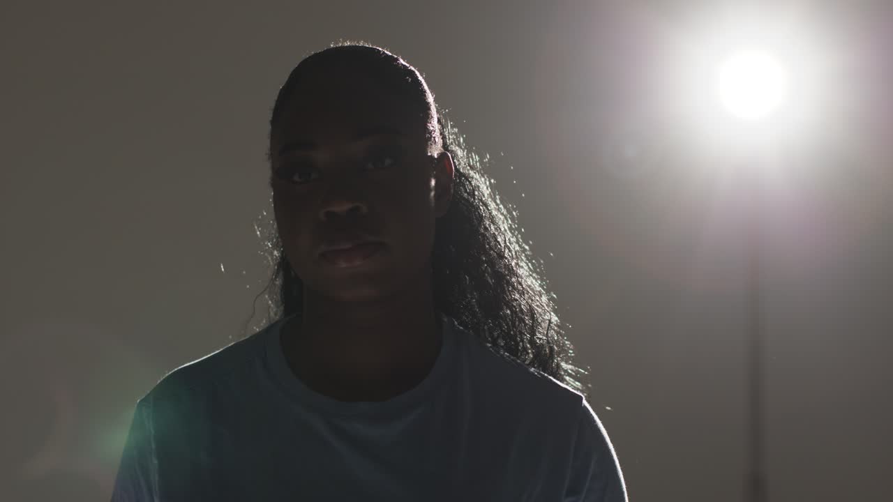 Backlit Head And Shoulders Studio Portrait Shot Of Young Woman With Low Key Lighting Against Grey Background
