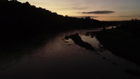 aerial: riverbank silhouette against golden pre-dawn sky, river flyover