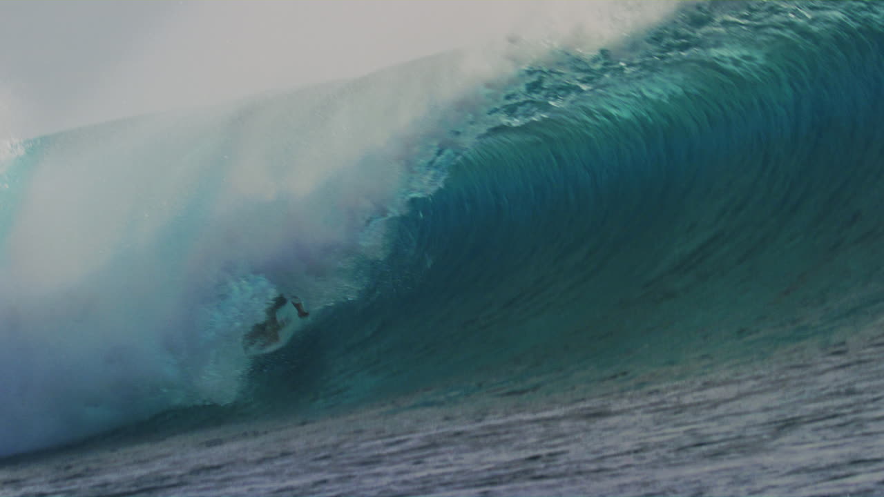 el surfista arrastra la mano a través del agua a medida que se adentran en el tubo del barril con el labio chocante y el cal