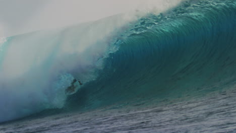 surfer drags hand across water as they get deep into barrel tube with crashing lip and whitewash