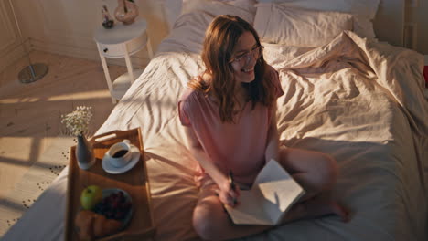 smiling girl writing book in morning. inspired carefree woman enjoying free time