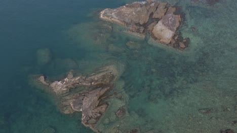 Vista-Aérea-De-Pájaro-Dolly-Shot-De-Rocas-De-Granito-Que-Salen-Del-Mar-Azul-Claro-Con-Arrecifes-De-Coral-Alrededor